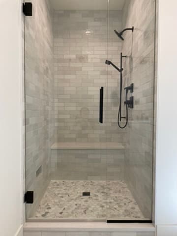 Frameless glass walk-in shower with gray subway tile, matte black fixtures, and a built-in bench