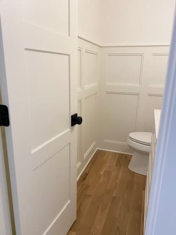 Powder room doorway view showing white paneled wainscoting and hardwood flooring