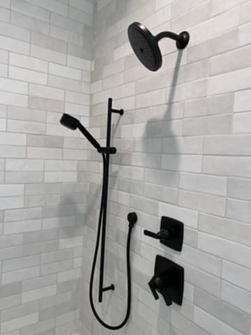 Close-up of matte black shower fixtures mounted on a gray subway tile wall