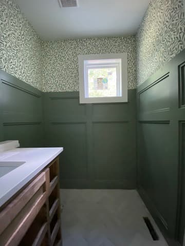 Bathroom with sage green wainscoting, leaf-print wallpaper, and herringbone tile flooring