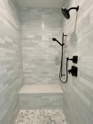 Walk-in shower featuring gray subway tile walls, a tile bench, and a pebble mosaic floor