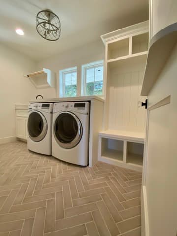 Laundry room with a curved built-in cubby nook, white cabinetry, and herringbone tile floor