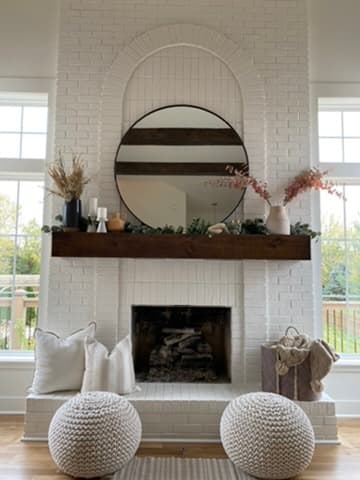 Painted brick fireplace with a stained wood mantel and round mirror