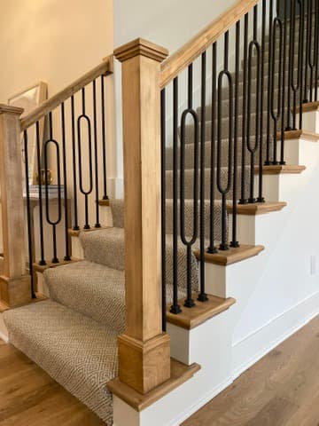 Staircase with custom wood railings, wrought iron balusters, and a patterned runner