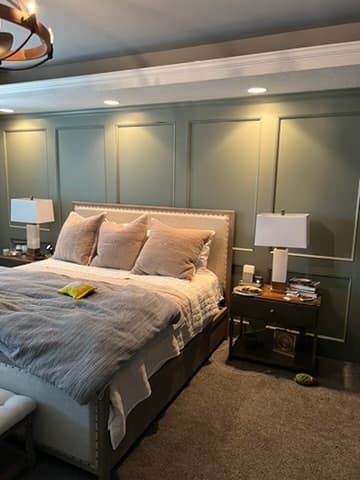 Primary bedroom accent wall with full-height sage green wood paneling and crown molding